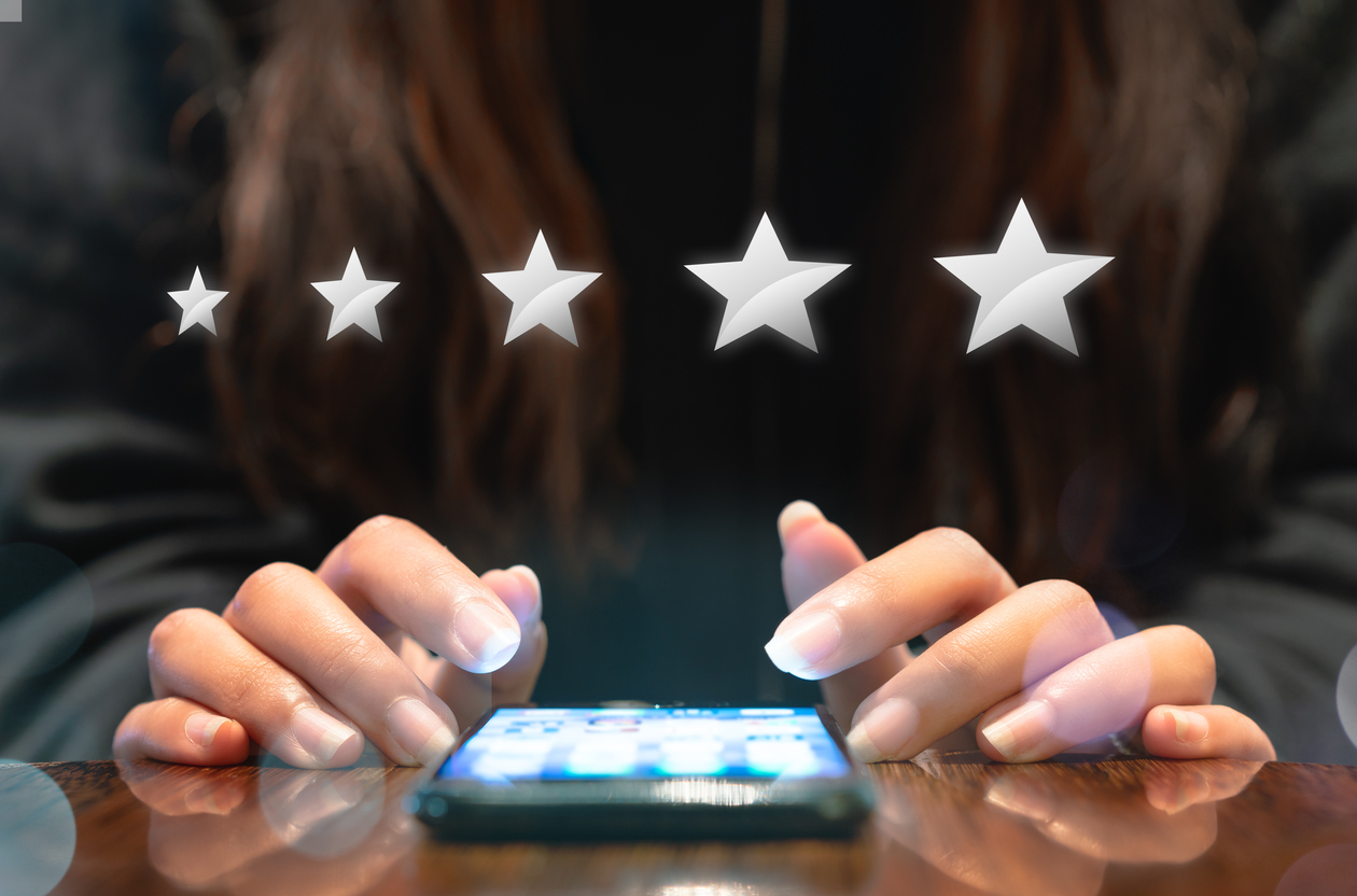 Women sitting at a table with a smartphone in front of her with five stars on the screen as she is reviewing customer experience analytics.