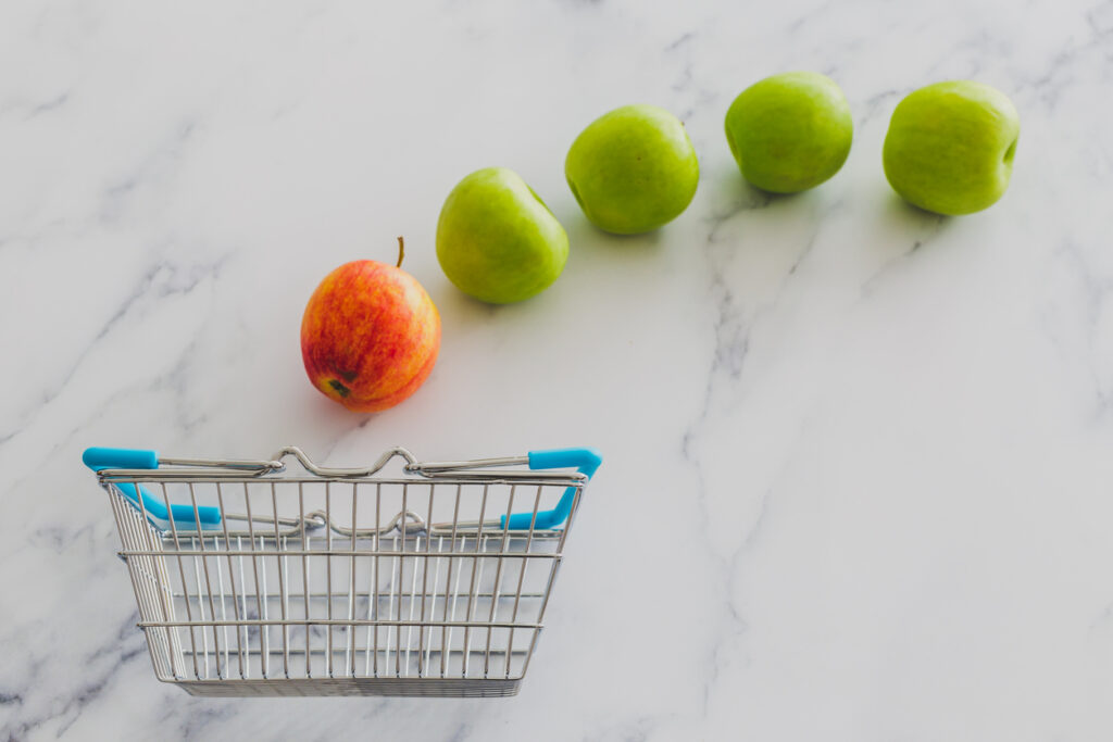 Product differentiation of a red apple compared to green apples as they fall into an empty grocery basket