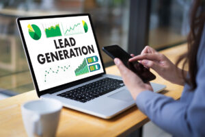 Person implementing sales lead tracking while holding a cell phone and sitting in front of a laptop that says "Lead Generation."